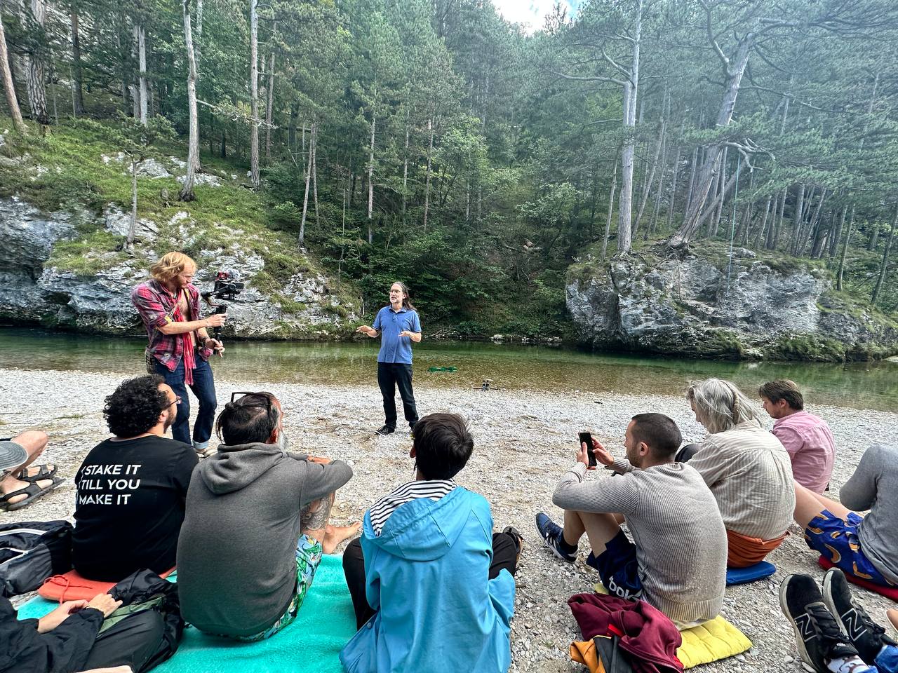 People sitting on rocks by a river during a discussion.